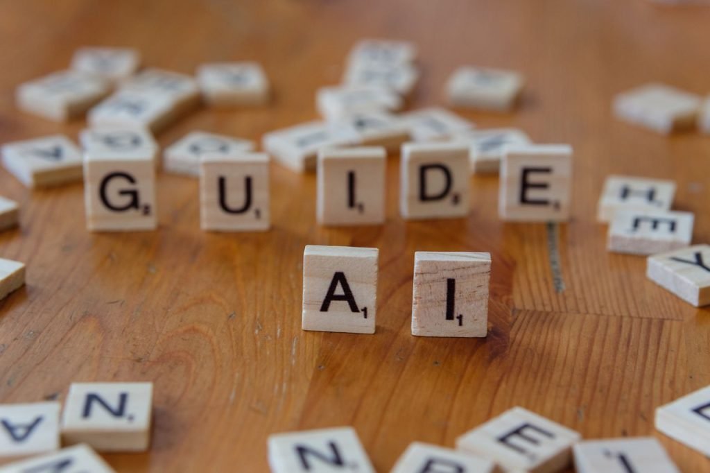 Scrabble letters spelling GUIDE and AI on a wooden surface, suggesting direction and technology.